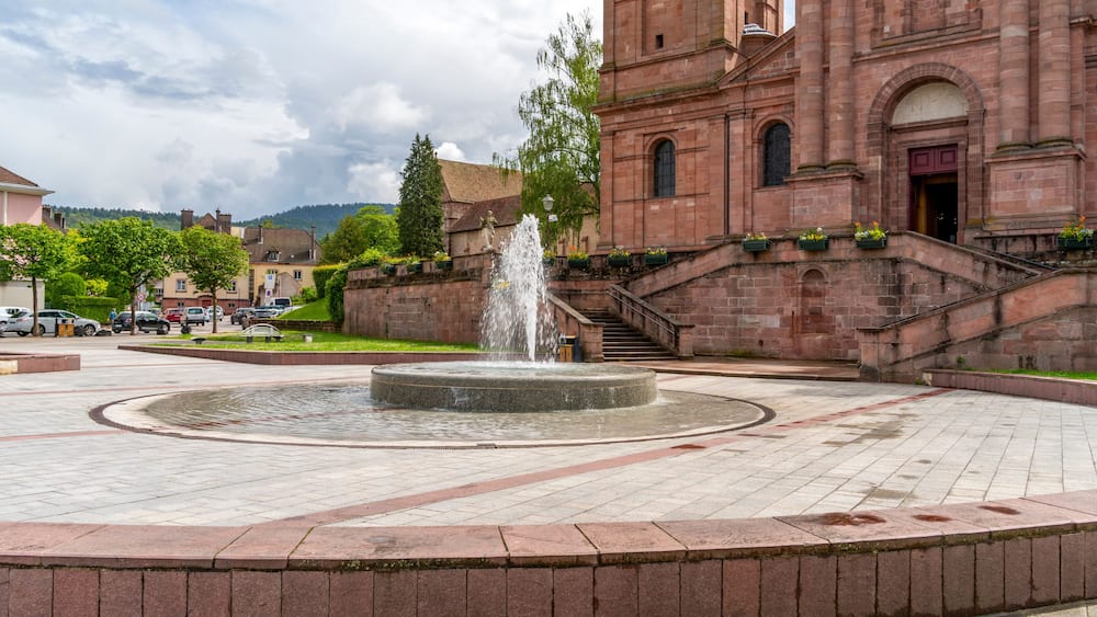 Eine historische Kirche mit einem Brunnen im Zentrum eines gepflasterten Platzes.