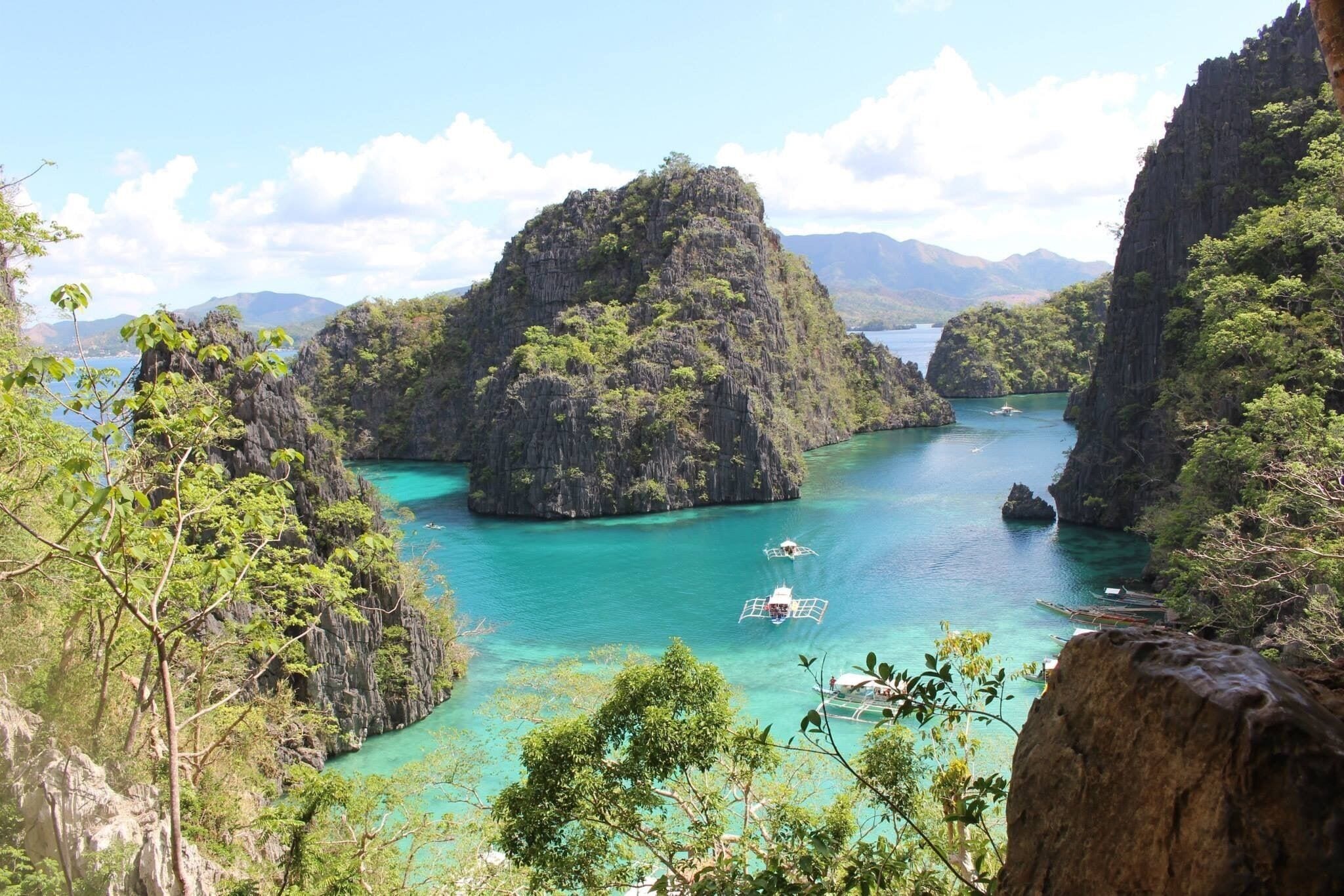A coastal landscape with a large rock formation surrounded by turquoise waters and lush greenery.