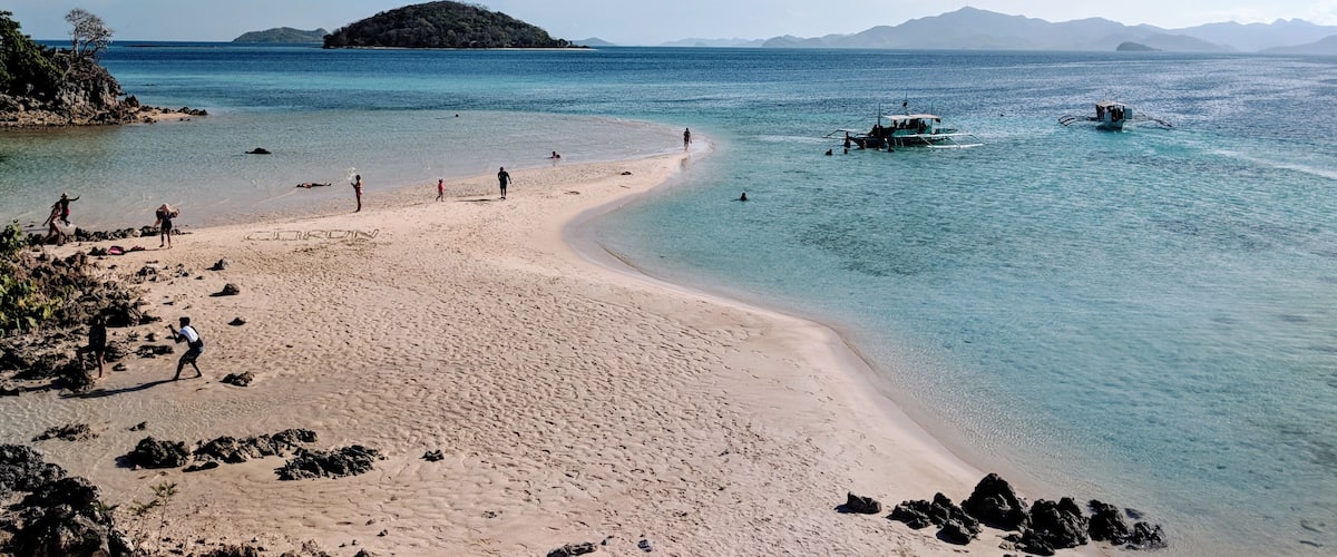 A beach with clear turquoise water, a sandy shore, and a small island in the distance.