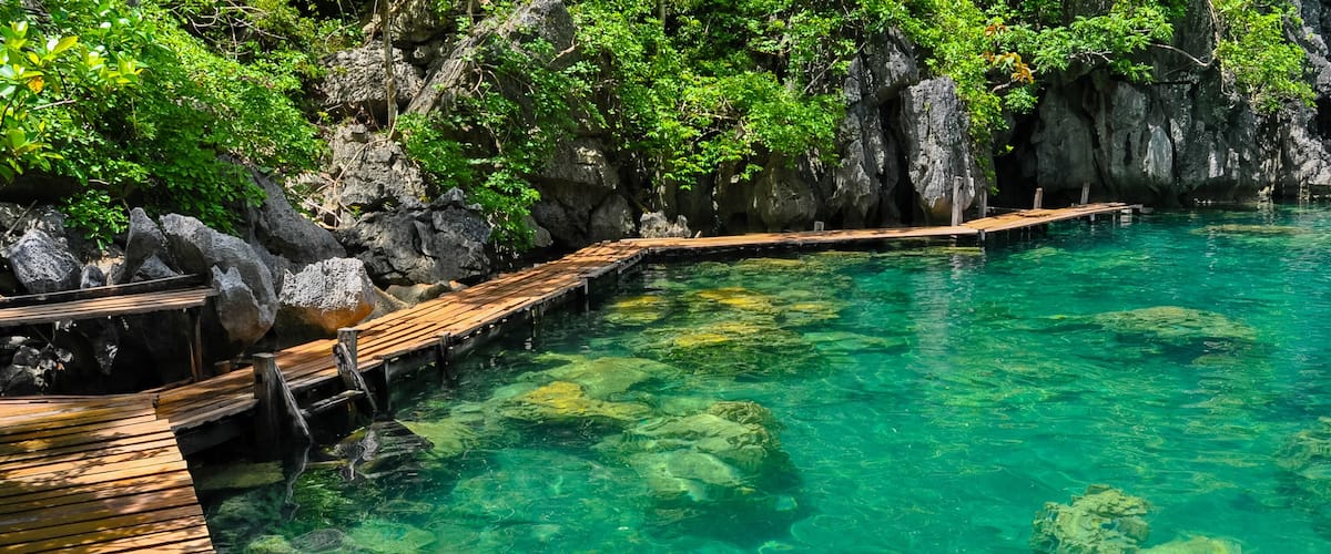 A wooden dock extending into clear turquoise water surrounded by rocky cliffs and lush greenery.