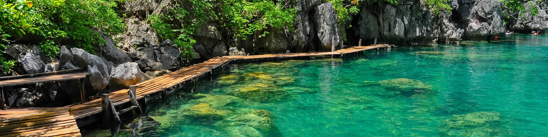 A wooden dock extending into clear turquoise water surrounded by rocky cliffs and lush greenery.