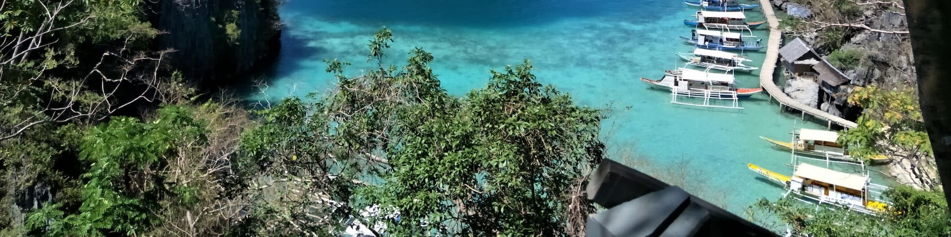 A coastal landscape with clear turquoise waters, rocky cliffs, and a dock with boats.