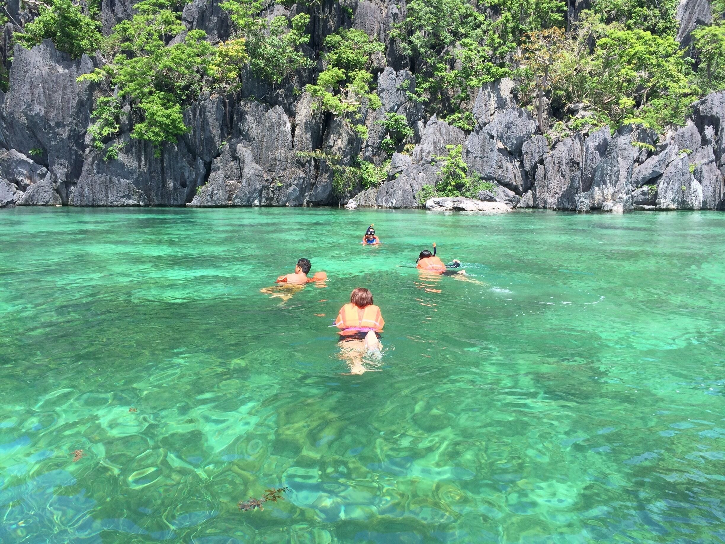 A clear turquoise sea with rocky cliffs and lush greenery in the background.