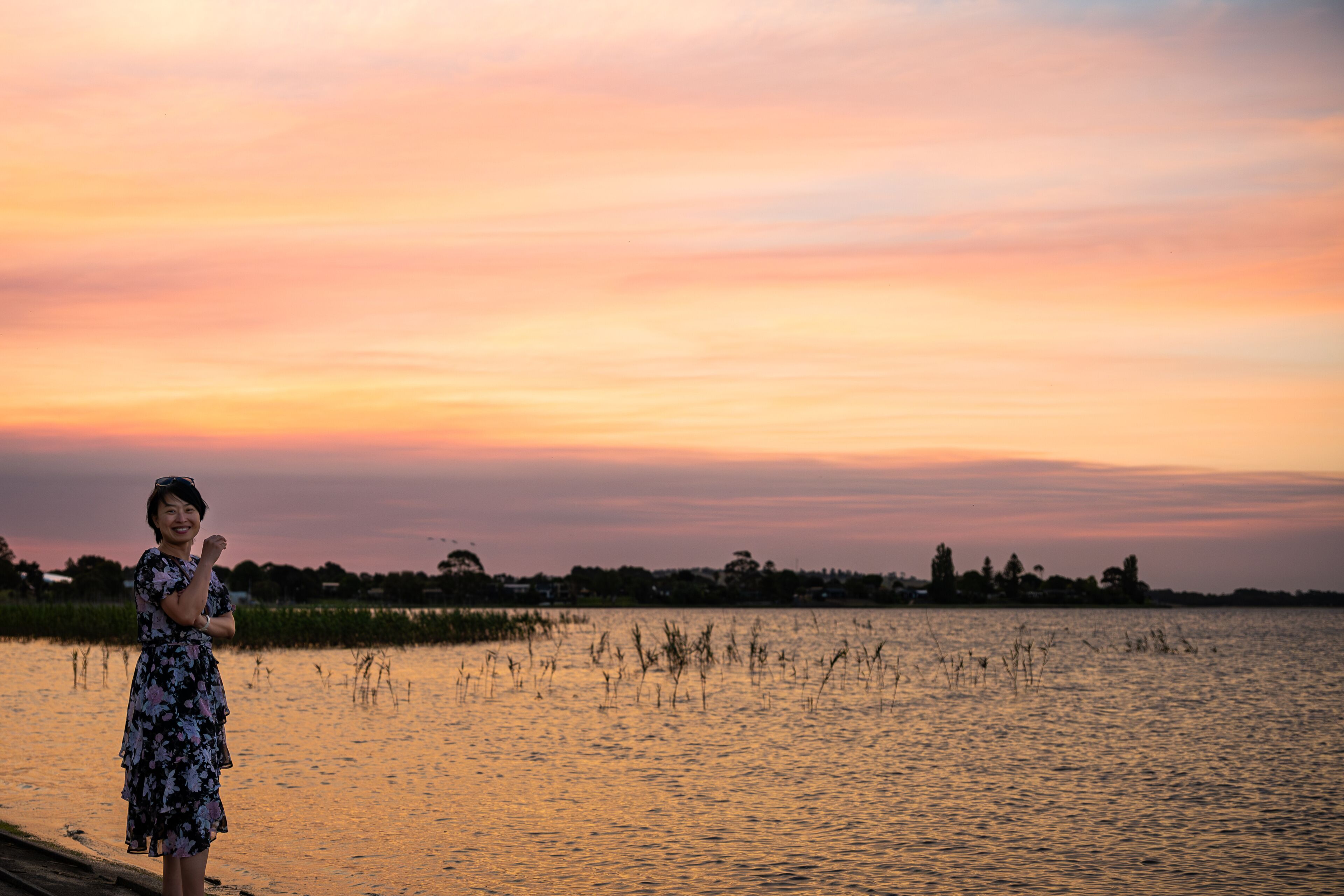 A woman by the lake enjoying the scenic view of the lake at dusk, with amazing sunset color above the sky, at Lake Colac, Colac, Victoria, Australia