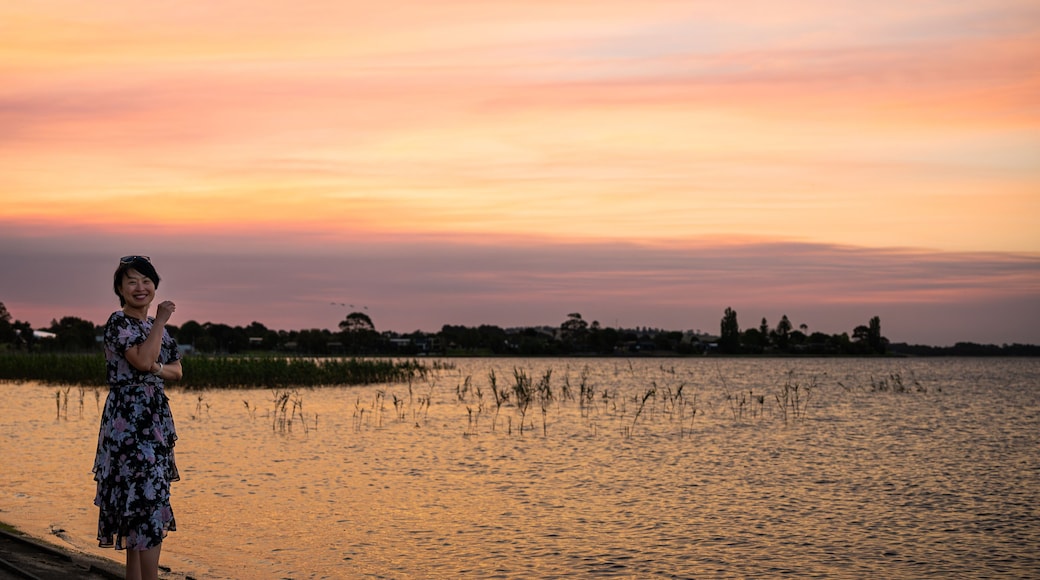 A woman by the lake enjoying the scenic view of the lake at dusk, with amazing sunset color above the sky, at Lake Colac, Colac, Victoria, Australia