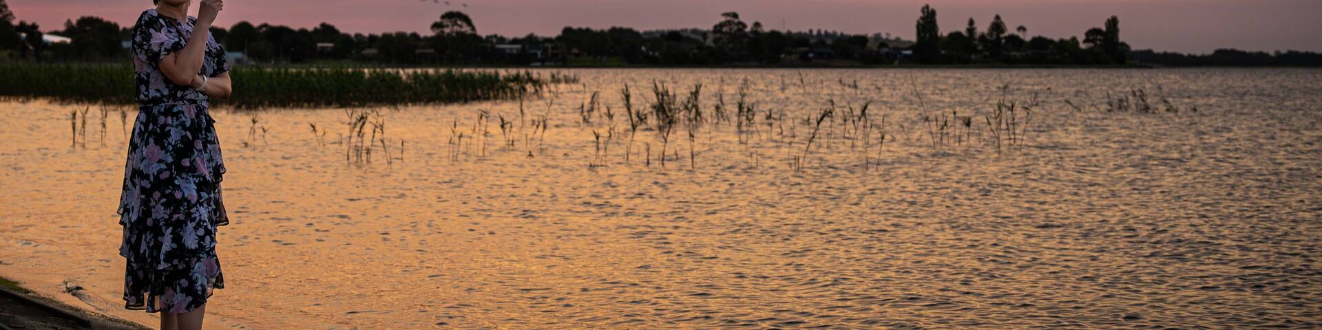 A woman by the lake enjoying the scenic view of the lake at dusk, with amazing sunset color above the sky, at Lake Colac, Colac, Victoria, Australia