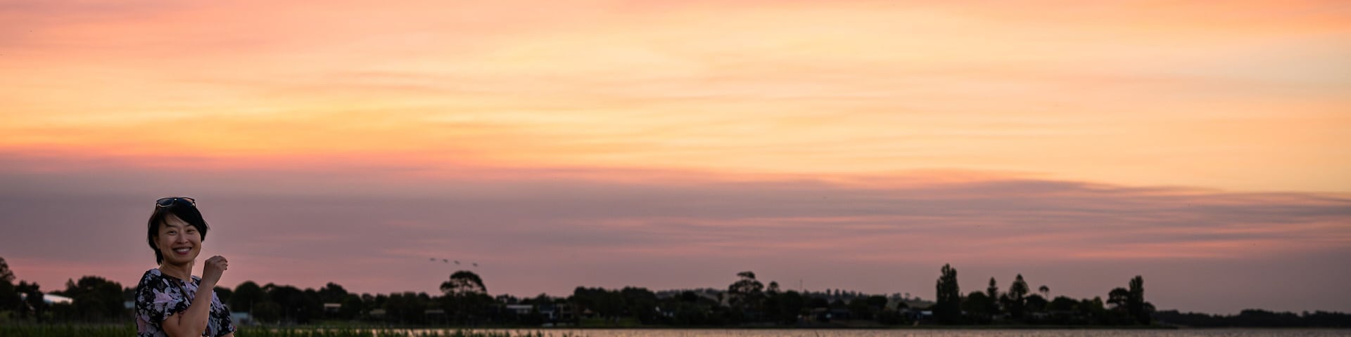 A woman by the lake enjoying the scenic view of the lake at dusk, with amazing sunset color above the sky, at Lake Colac, Colac, Victoria, Australia