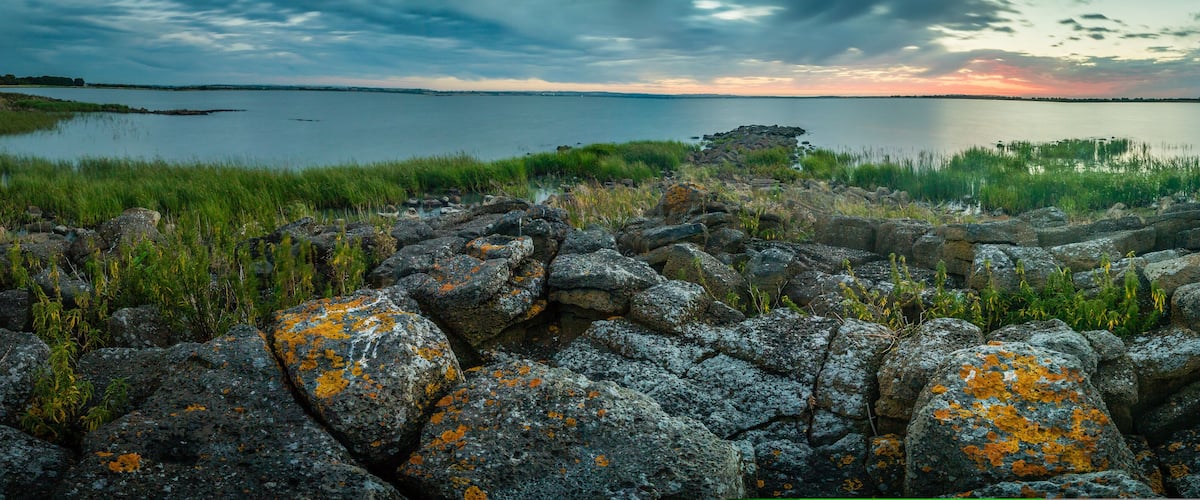 A rocky shoreline with lichen-covered rocks and a calm lake at sunset.
