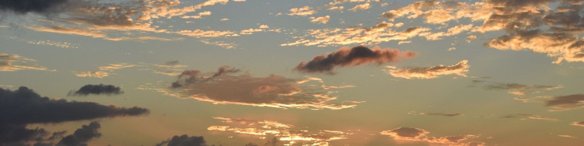 A sunset over a calm sea with scattered clouds.