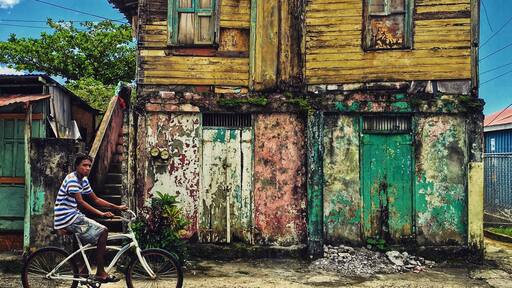 Outside of the centre of Roseau kid cruising by a house that seems desolated. When I wanted to look inside it turned out to be occupied and man was watching tv.