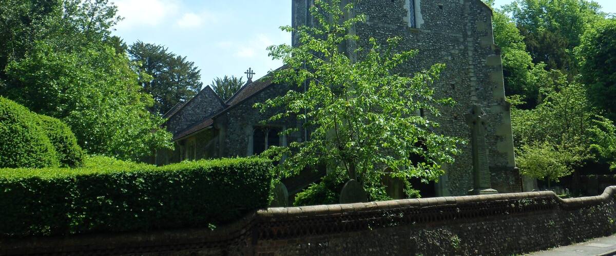 A historic stone tower with a clock, surrounded by lush greenery and a stone wall.