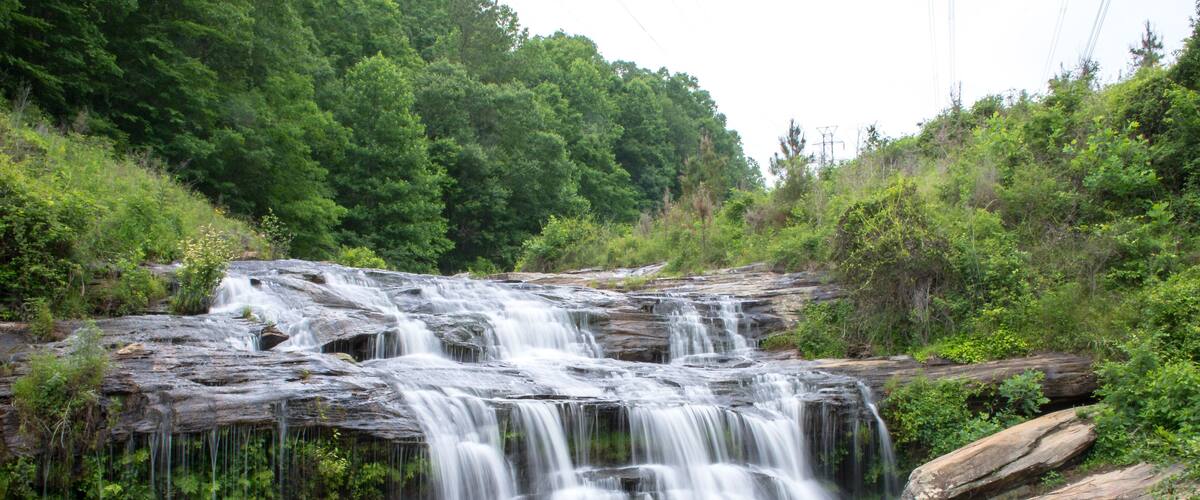 A waterfall cascading over a rocky ledge into a calm river surrounded by lush greenery.