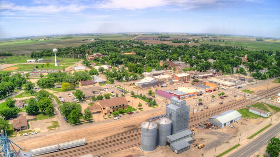 An aerial view of a small town with a train station, industrial buildings, and surrounding farmland.