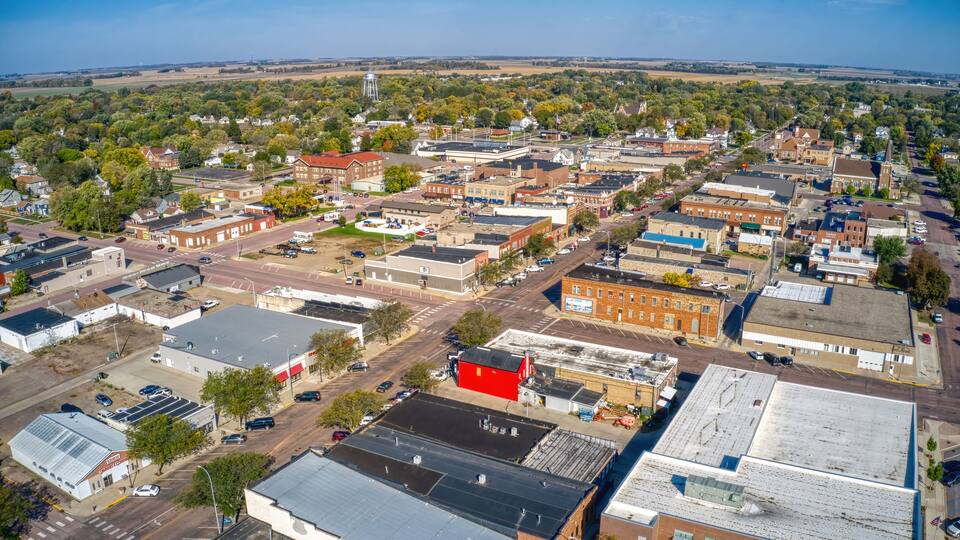 An aerial view of a small town with a mix of residential and commercial buildings, a prominent water tower, and a church steeple.