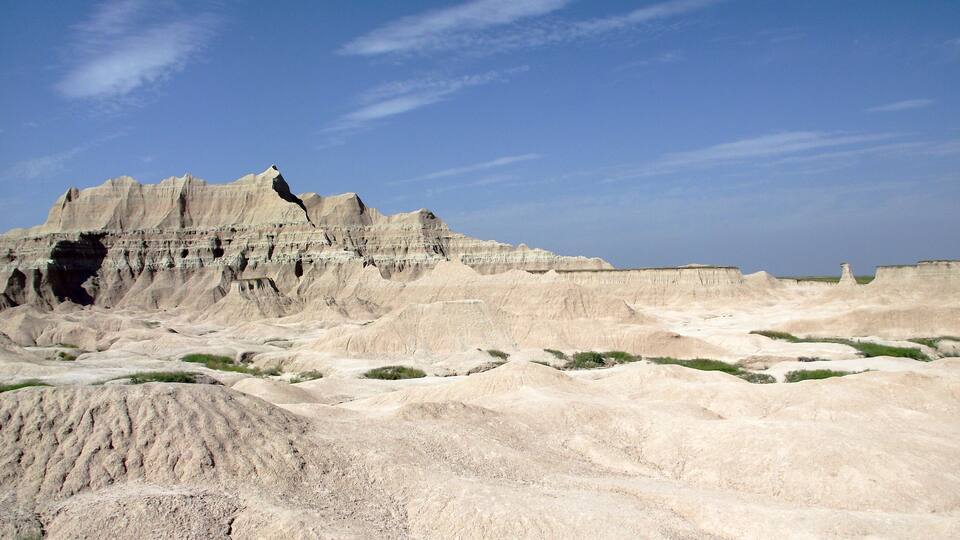 A vast, rugged landscape with layered sedimentary rock formations and sparse vegetation.