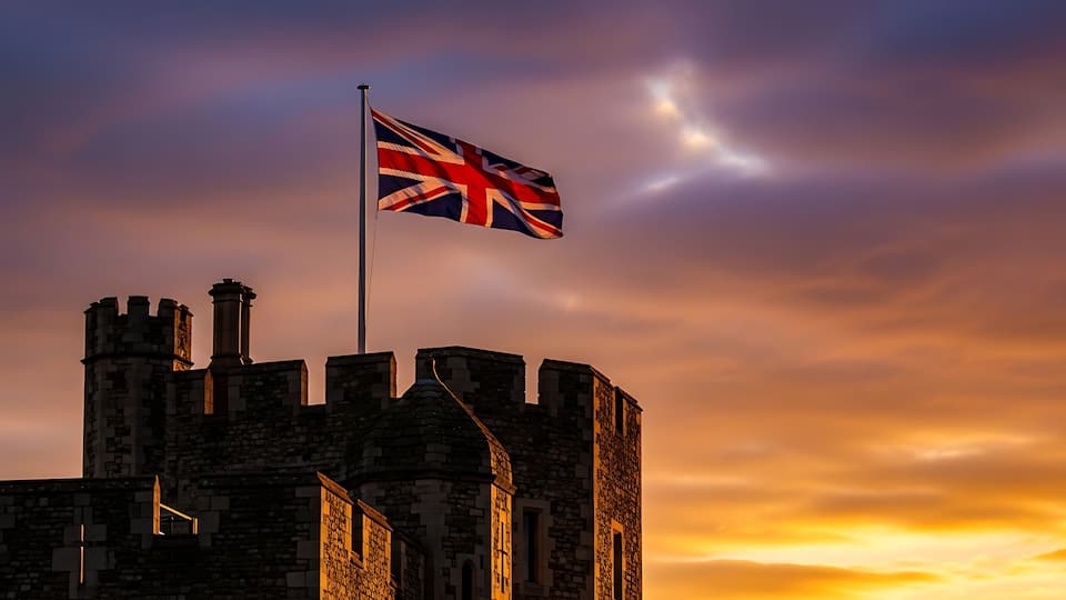 A historic stone building with a flagpole and a flag, set against a sunset sky.