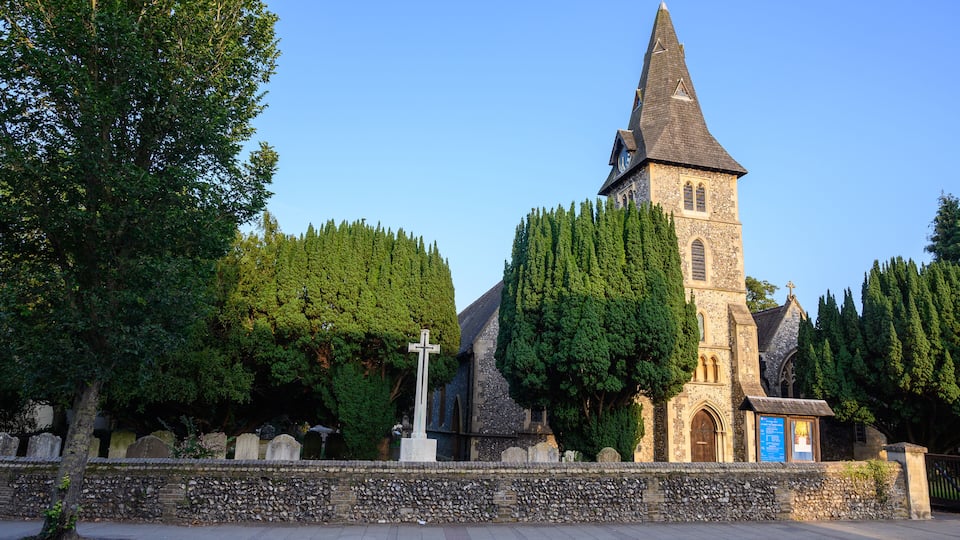 A church with a tall steeple, surrounded by trees and a stone wall.