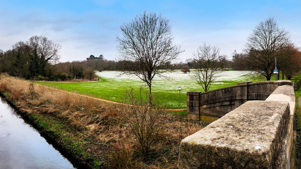 A canal, a stone bridge, and a green field with trees.