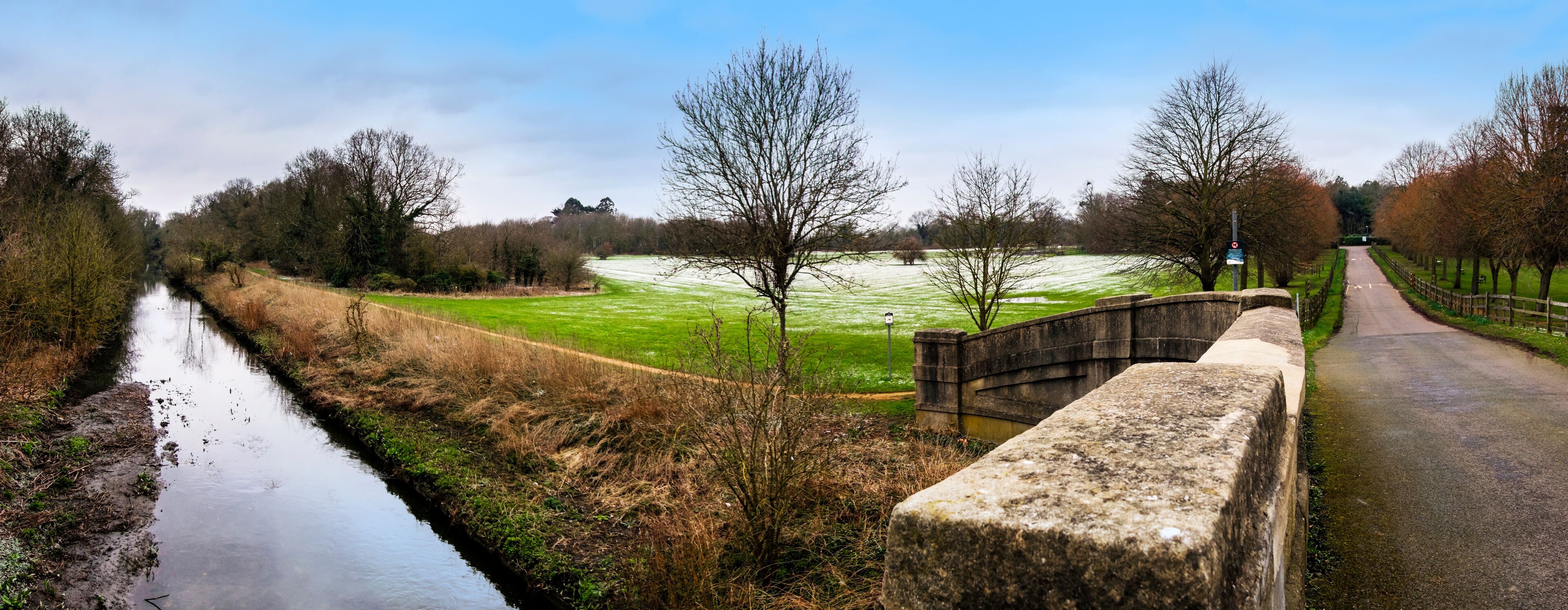 A canal, a stone bridge, and a green field with trees.