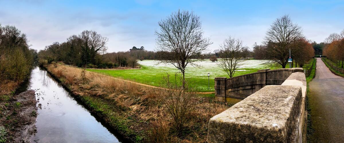 A canal, a stone bridge, and a green field with trees.