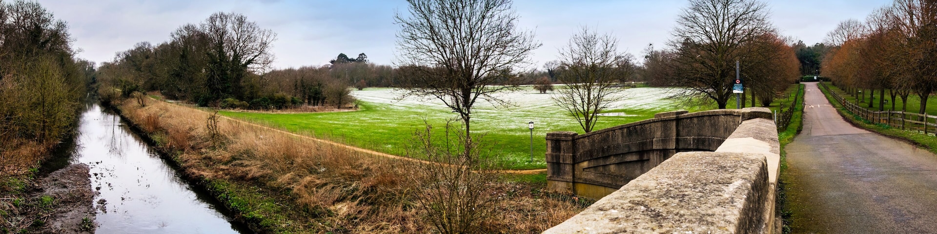 A canal, a stone bridge, and a green field with trees.