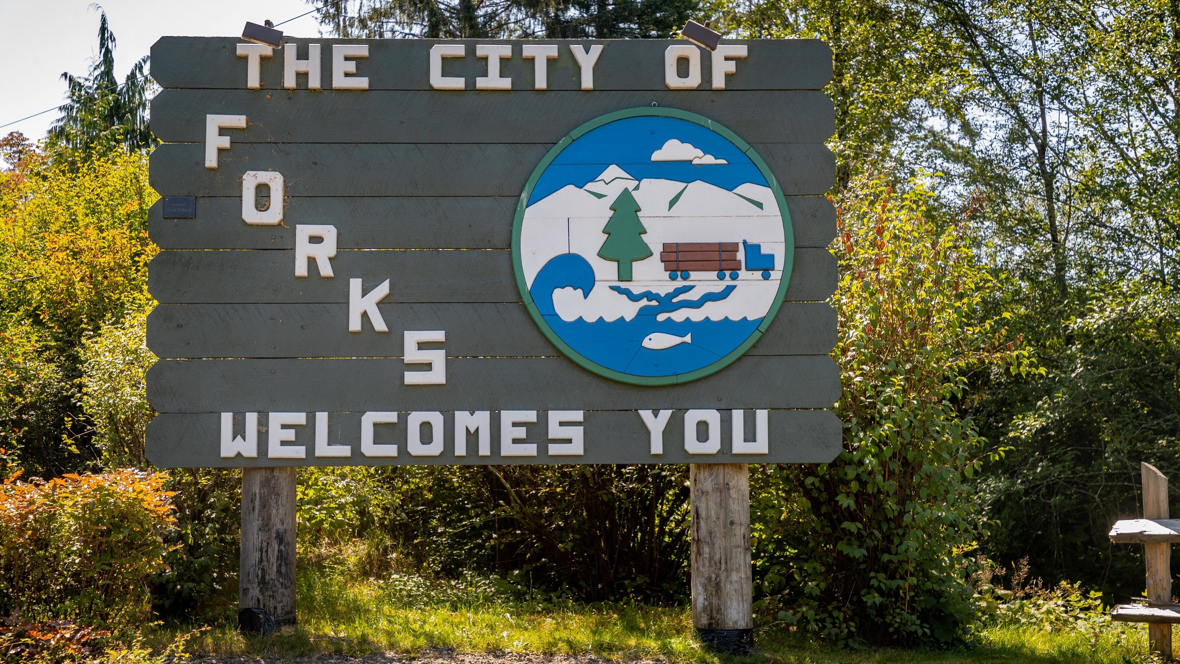 A welcome sign for the City of Forks with a logo featuring mountains, a tree, a truck, and a fish.