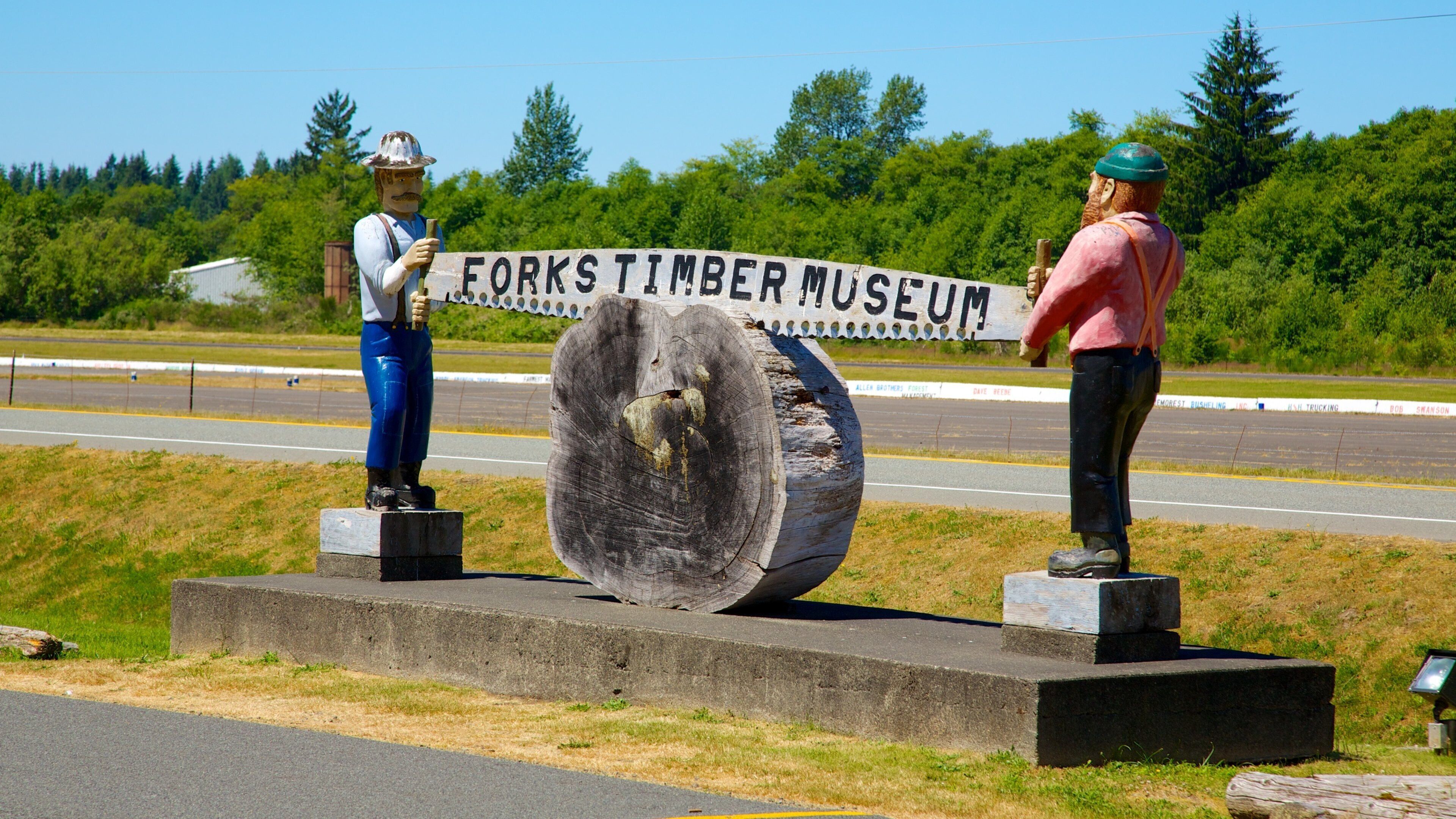Two statues of lumberjacks in front of a sign for the Forks Timber Museum.