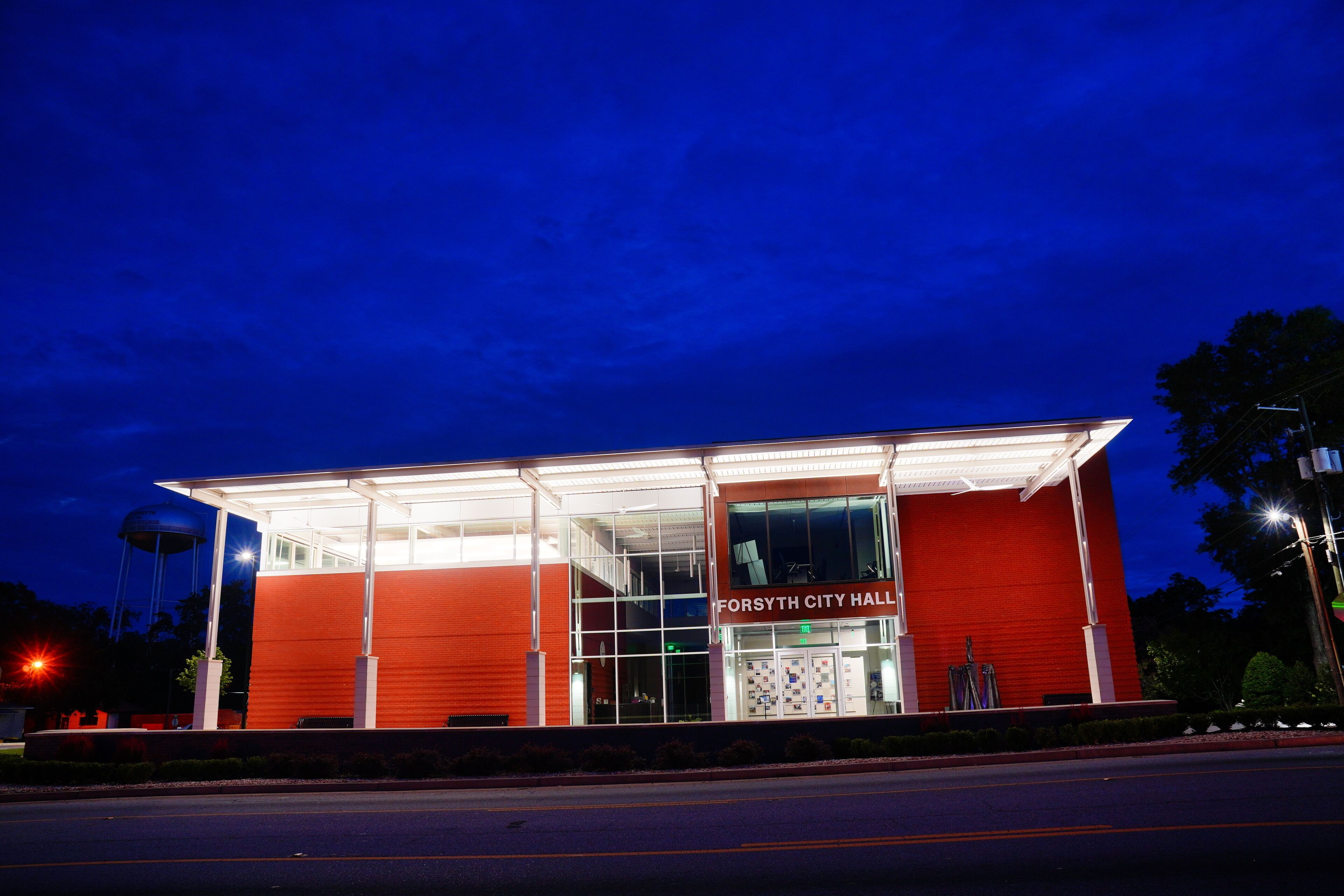 A red building with a glass facade and the sign "Forsyth City Hall" at night.