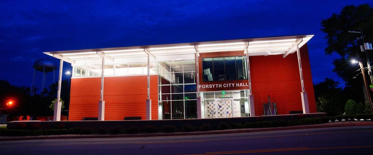 A red building with a glass facade and the sign "Forsyth City Hall" at night.