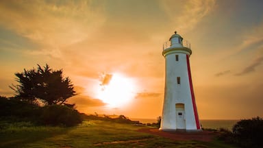 Un faro con una banda roja, silueteado contra un cielo de atardecer.