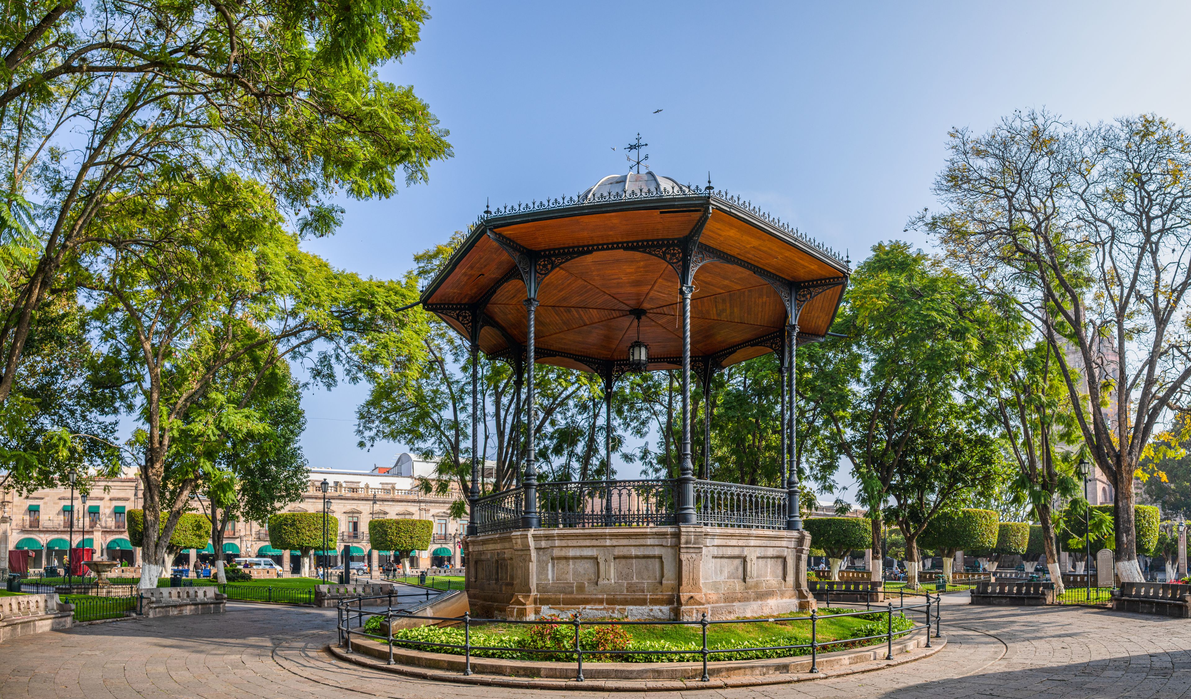 A gazebo with a dome roof, surrounded by trees and a fountain in a park.
