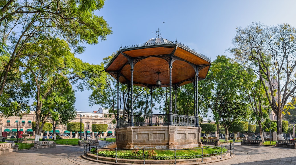 A gazebo with a dome roof, surrounded by trees and a fountain in a park.