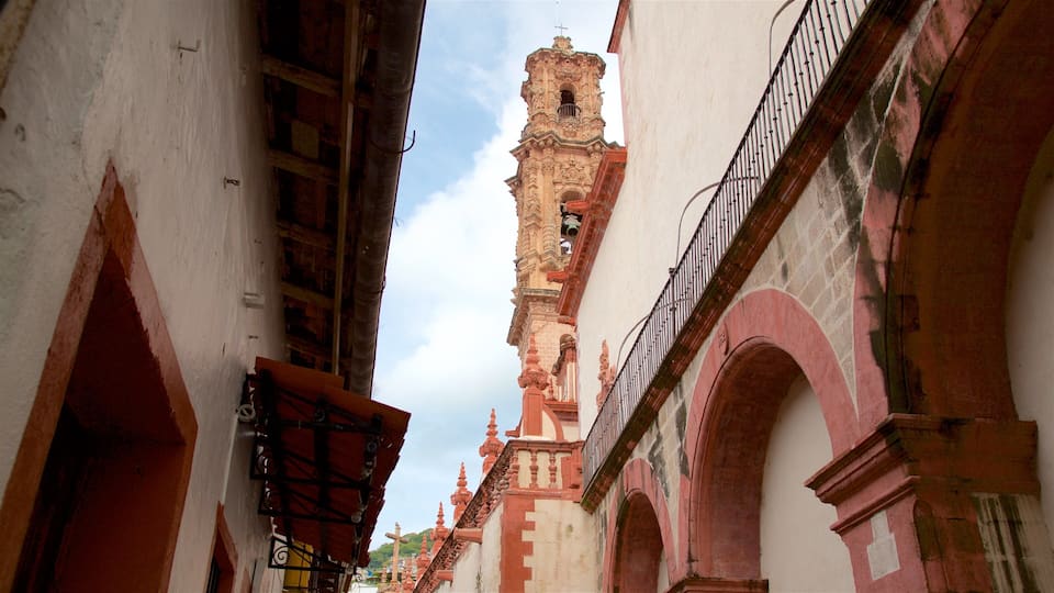 A narrow street with ornate buildings, a prominent bell tower, and a cross on top.