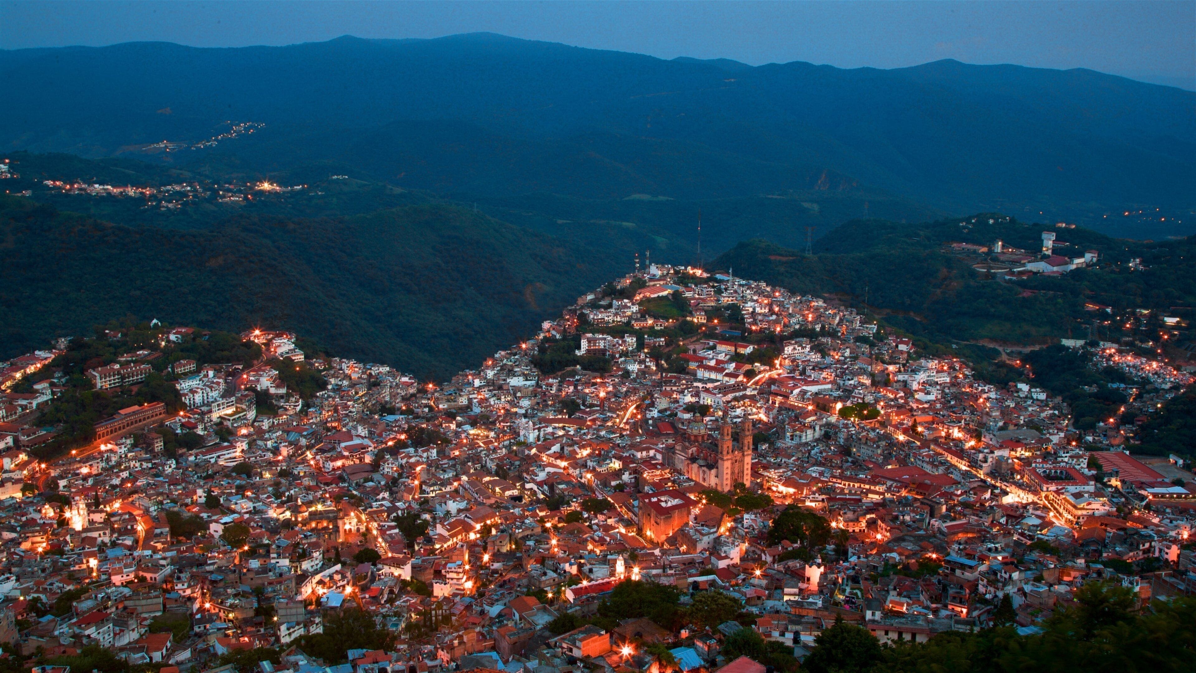 A densely populated town with a prominent church tower, surrounded by hills and mountains.