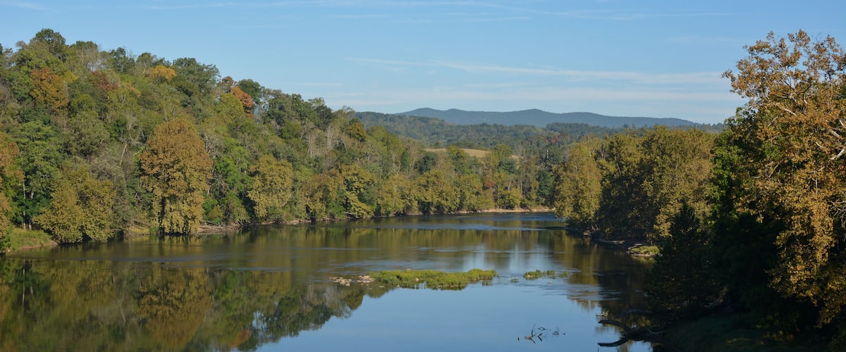 A calm lake surrounded by dense forest and distant mountains.