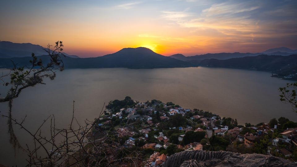 A sunset over a lake with a town in the foreground and mountains in the background.