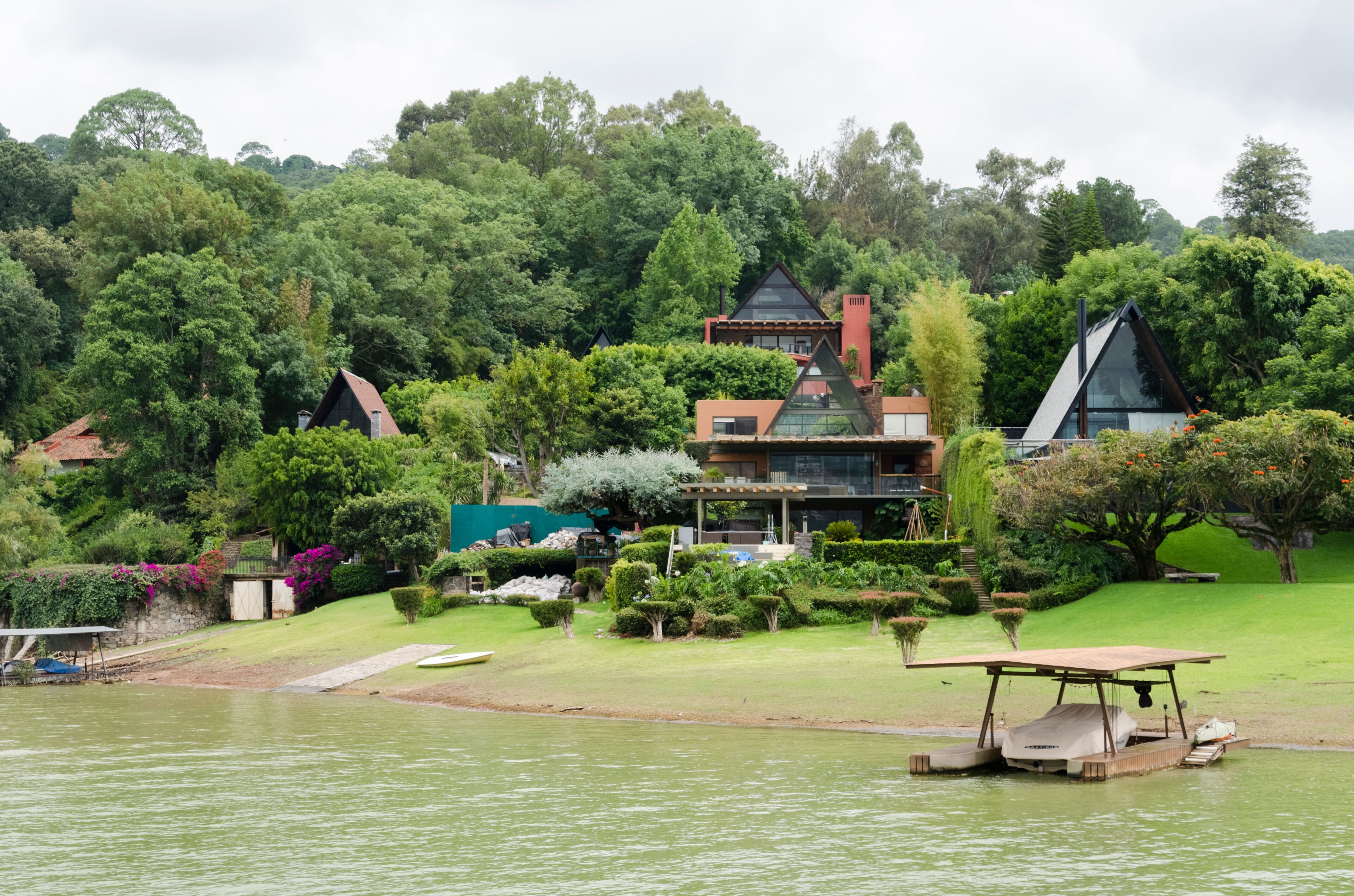 A lakeside house with a boat dock, surrounded by lush greenery and trees.