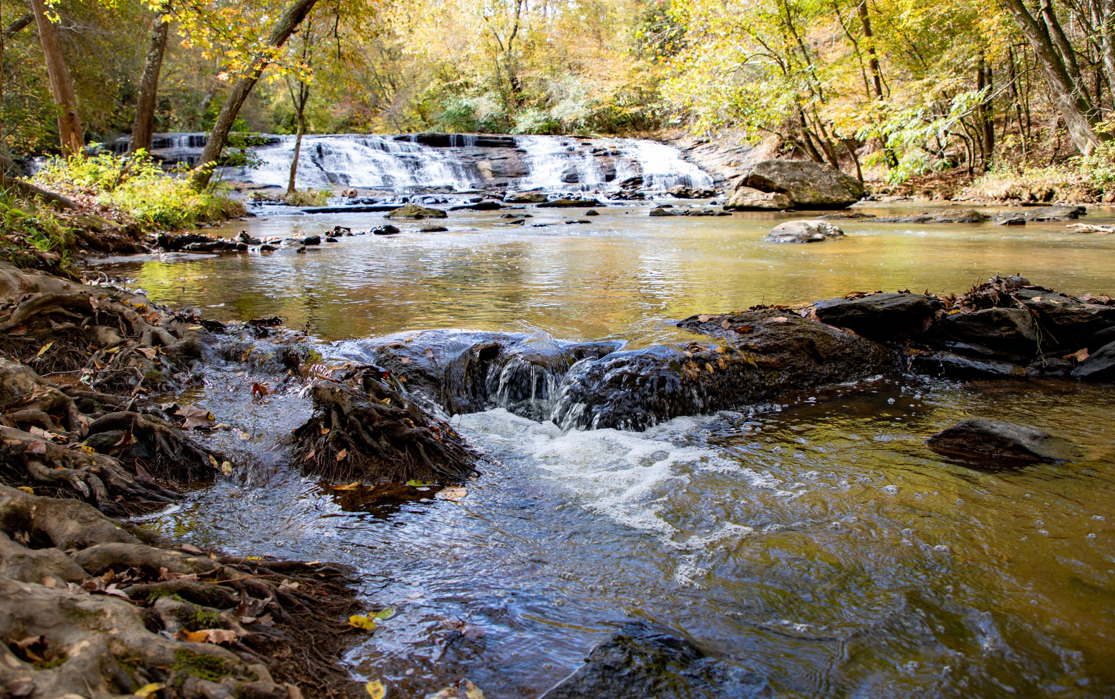 A waterfall in a forest with rocks and autumn leaves.