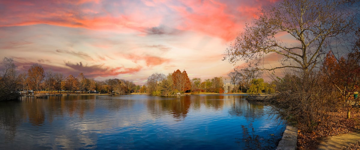 a stunning panoramic shot of the blue waters of the lake in the park surrounded by gorgeous autumn colored trees reflecting off the lake at sunset at Centennial Park in Nashville Tennessee USA
