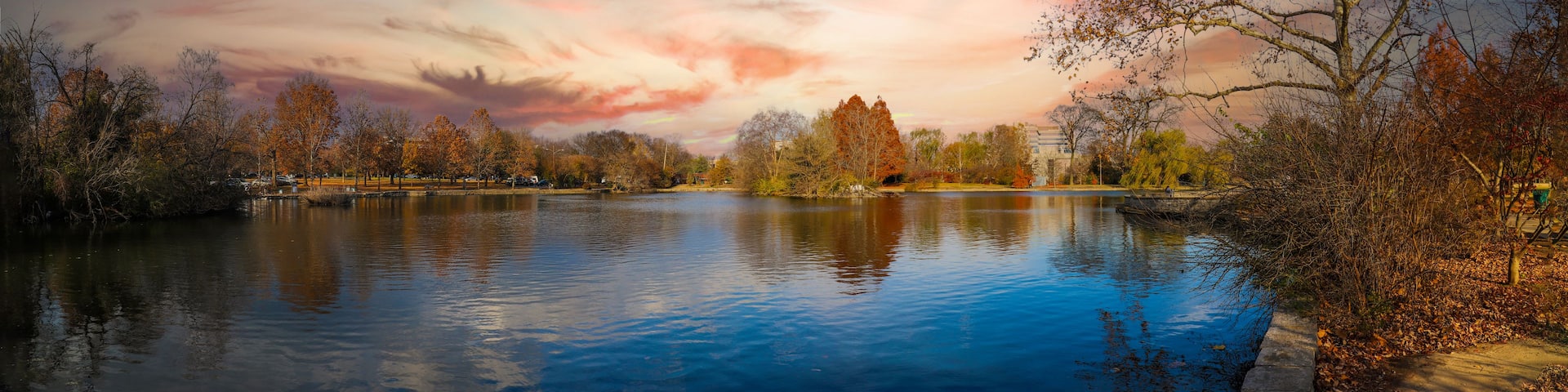 a stunning panoramic shot of the blue waters of the lake in the park surrounded by gorgeous autumn colored trees reflecting off the lake at sunset at Centennial Park in Nashville Tennessee USA