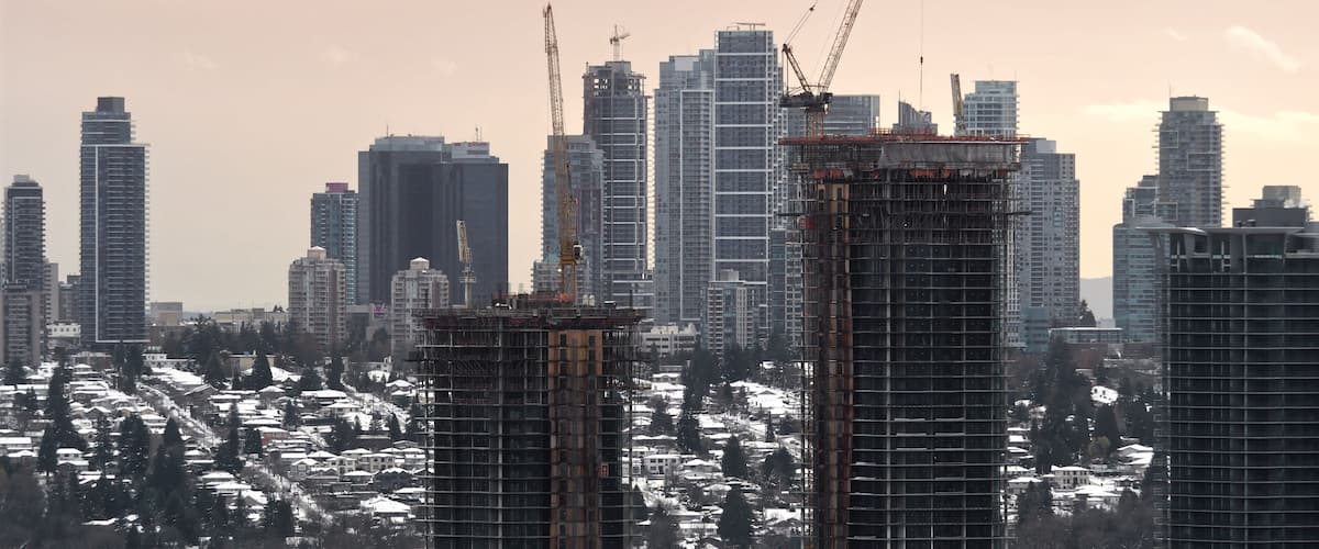 A cityscape with high-rise buildings, construction cranes, and snow-covered houses.