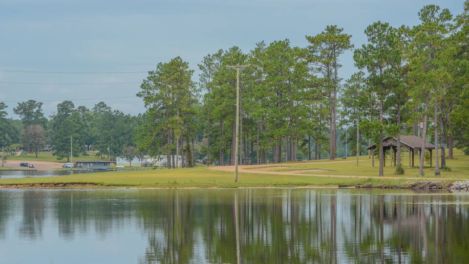A tranquil lakeside scene with a gazebo, a boat dock, and a golf course in the background.