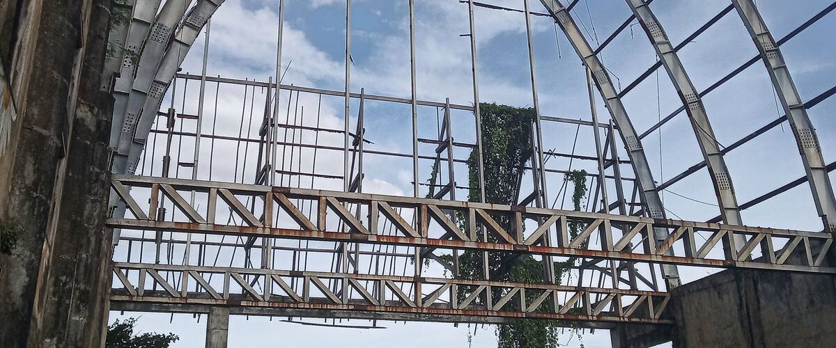 A large metal framework with a curved roof, surrounded by dense green foliage.