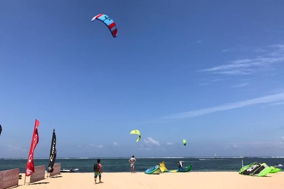 Una playa con cometas volando, banderas y un cielo despejado.