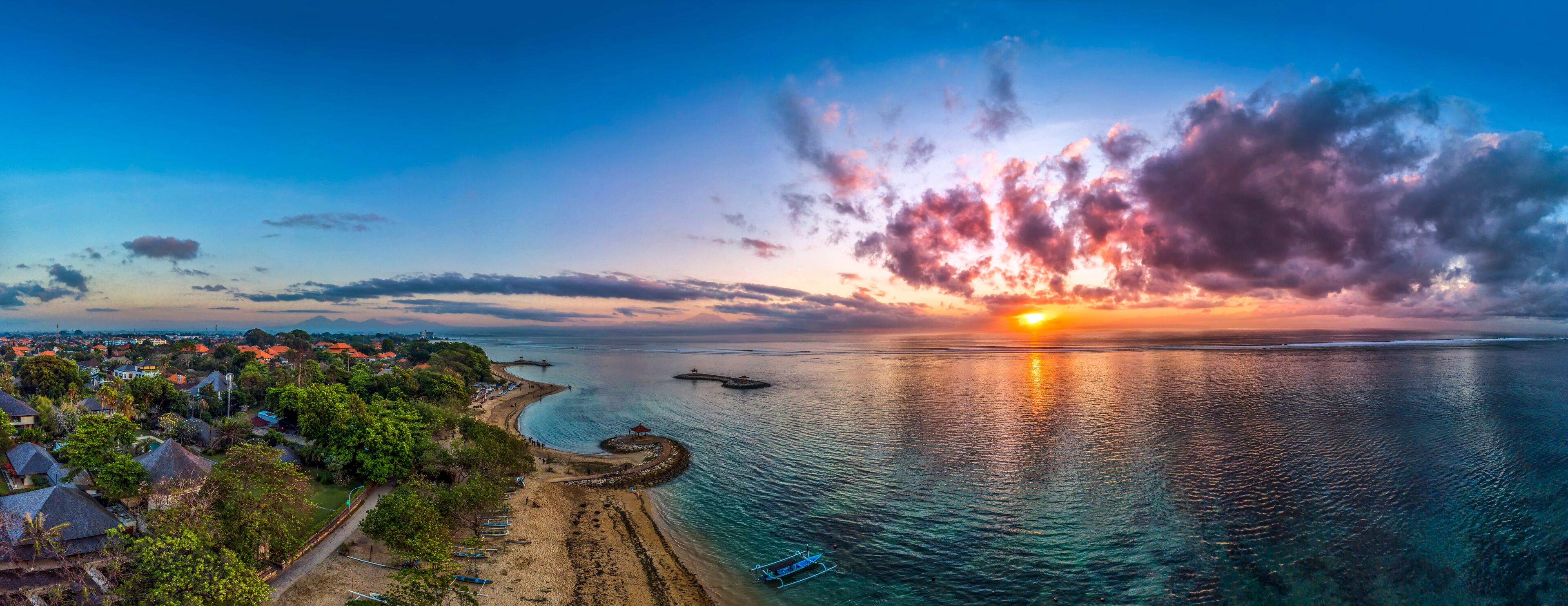 A coastal sunset with a beach, houses, and boats.