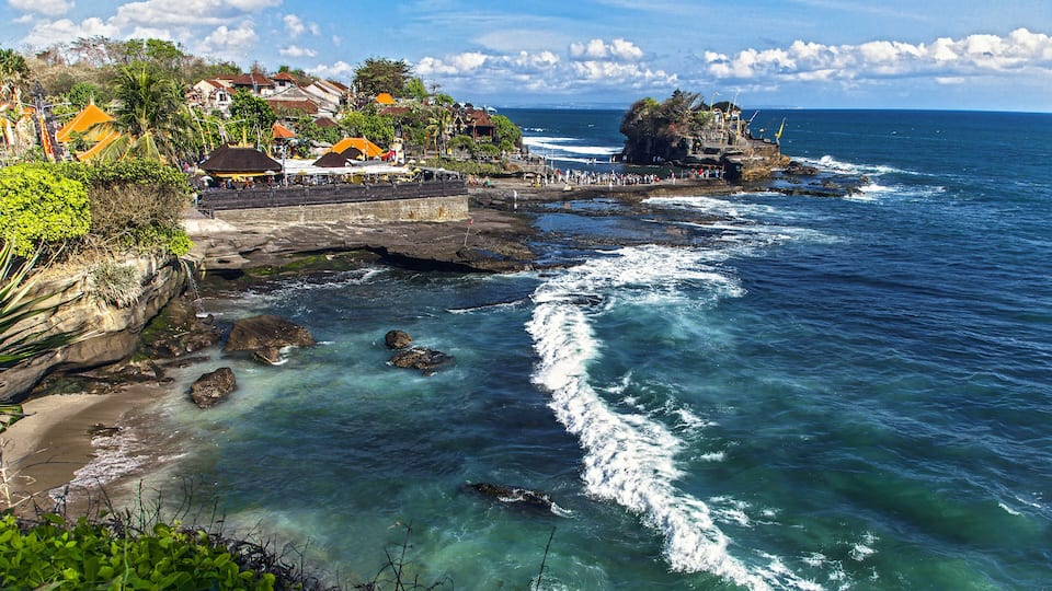 A coastal town with a rocky shoreline, clear blue waters, and a prominent rock formation.
