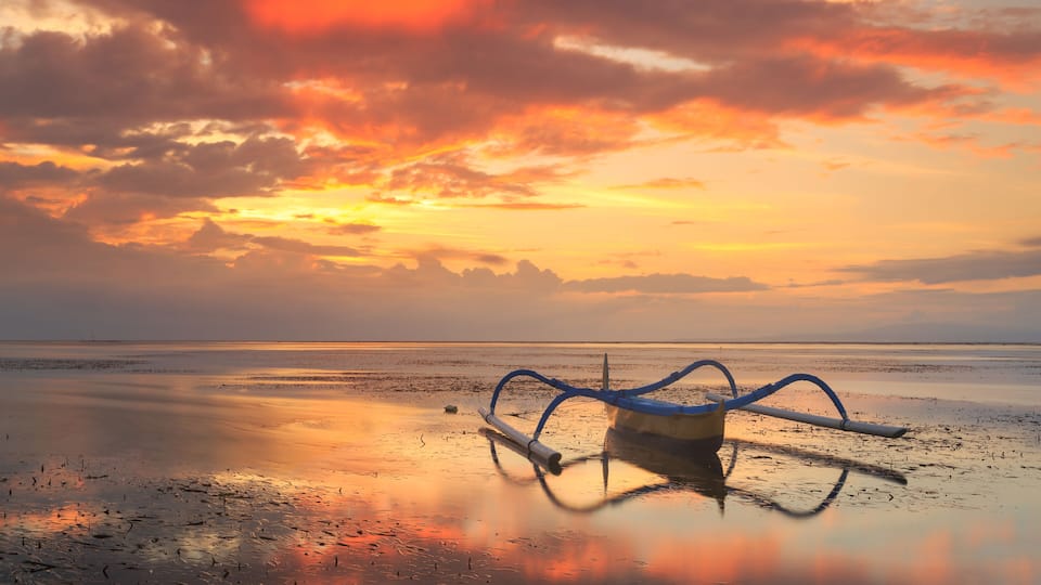 A sunset over a calm beach with a blue kayak in the foreground.