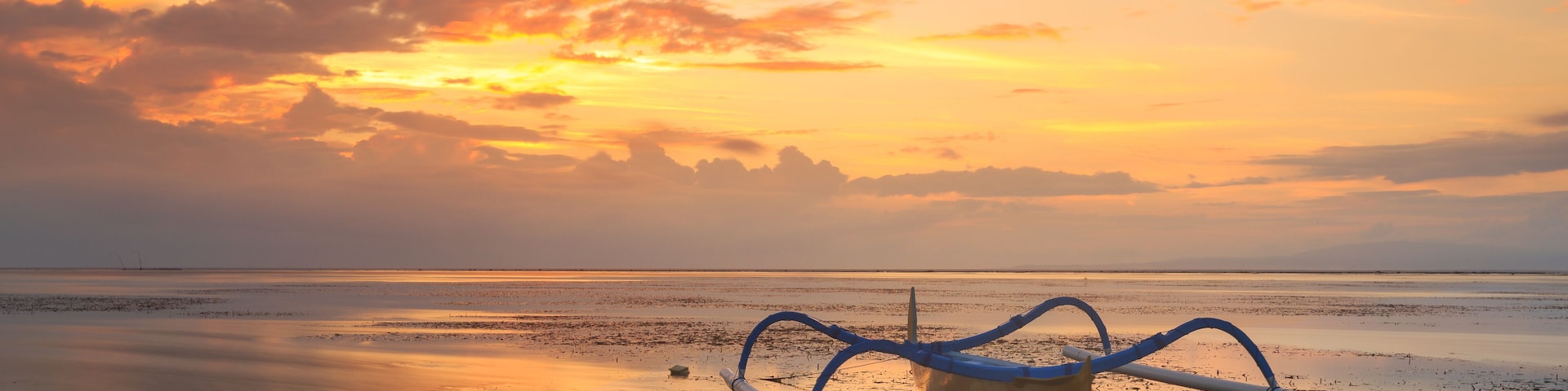 Un atardecer sobre una playa tranquila con un kayak azul en primer plano.