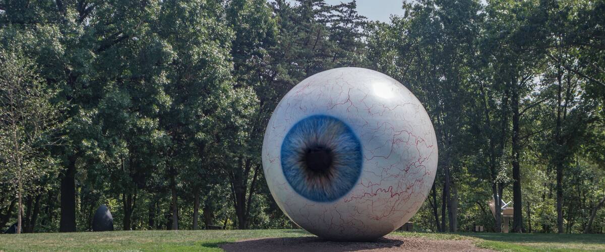 A large eye sculpture in a park surrounded by trees.