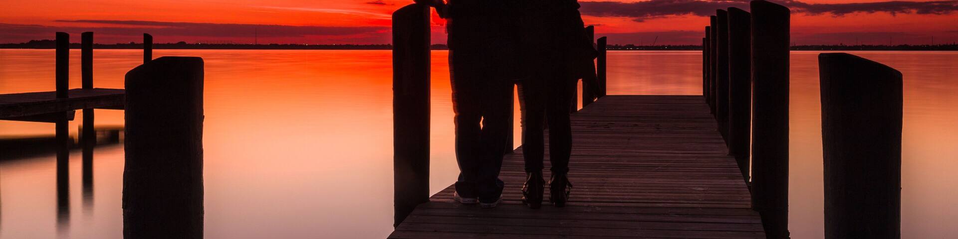 A wooden pier extending into calm water at sunset with a vibrant sky.